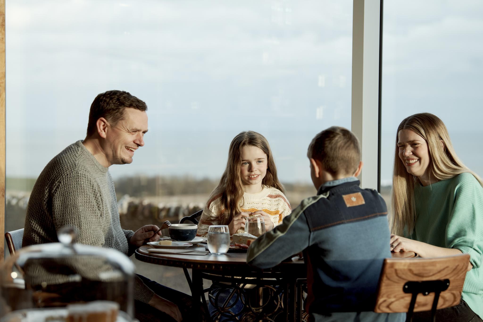 Two parents and two children sit around a table eating lunch.