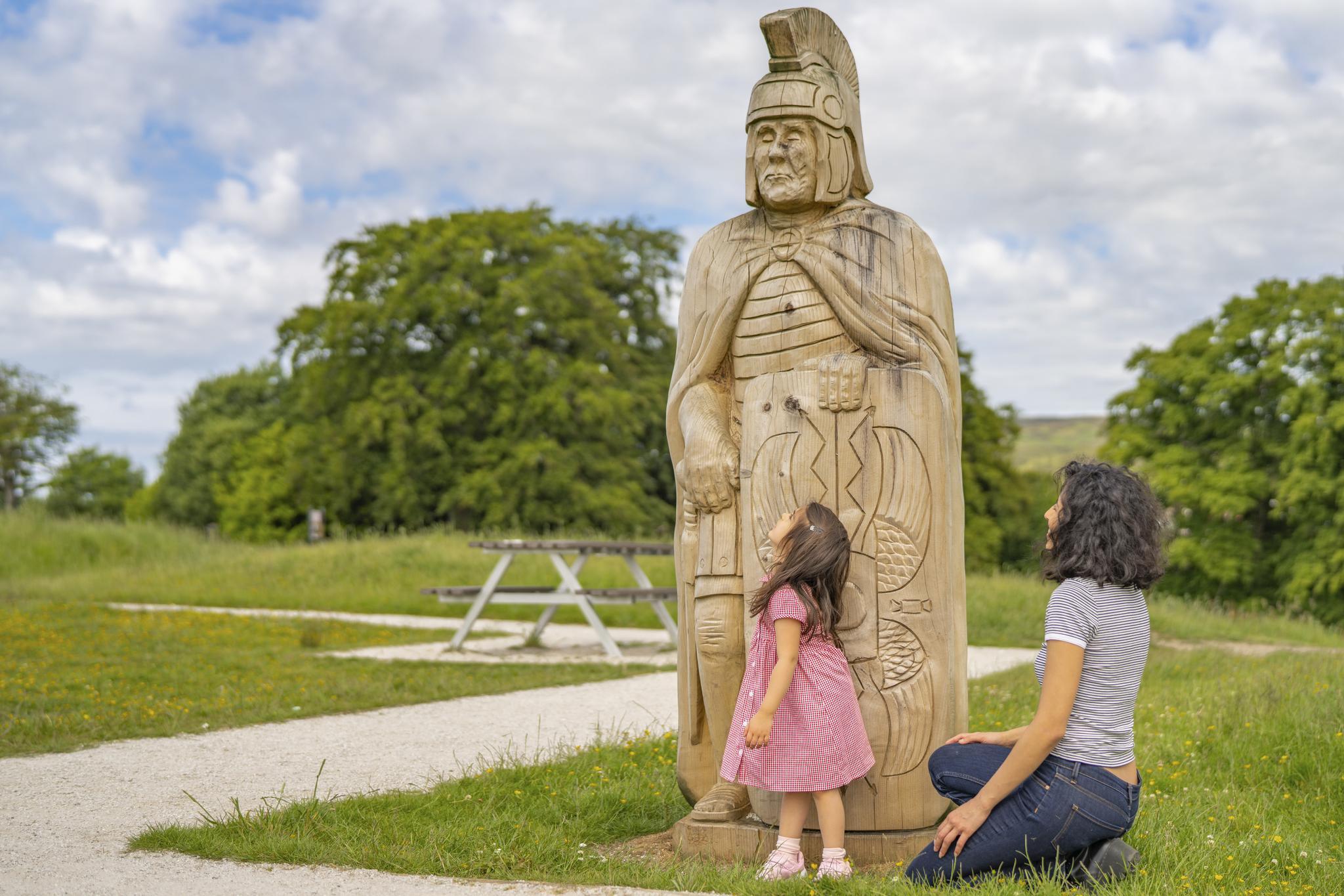 Mother and daughter look up at wooden statue of a Roman centurion