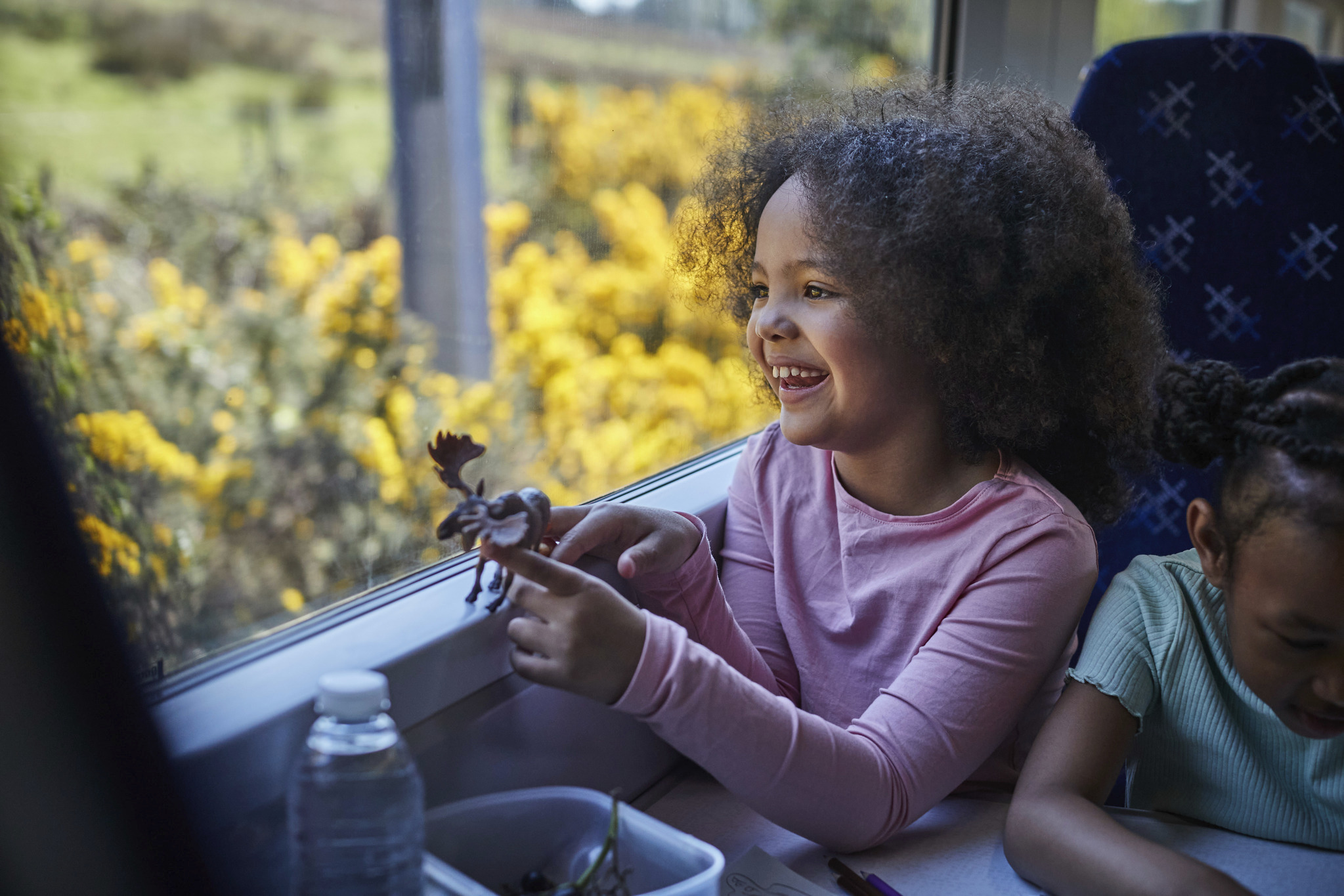 Little girl plays with a toy moose in looking out of a train window
