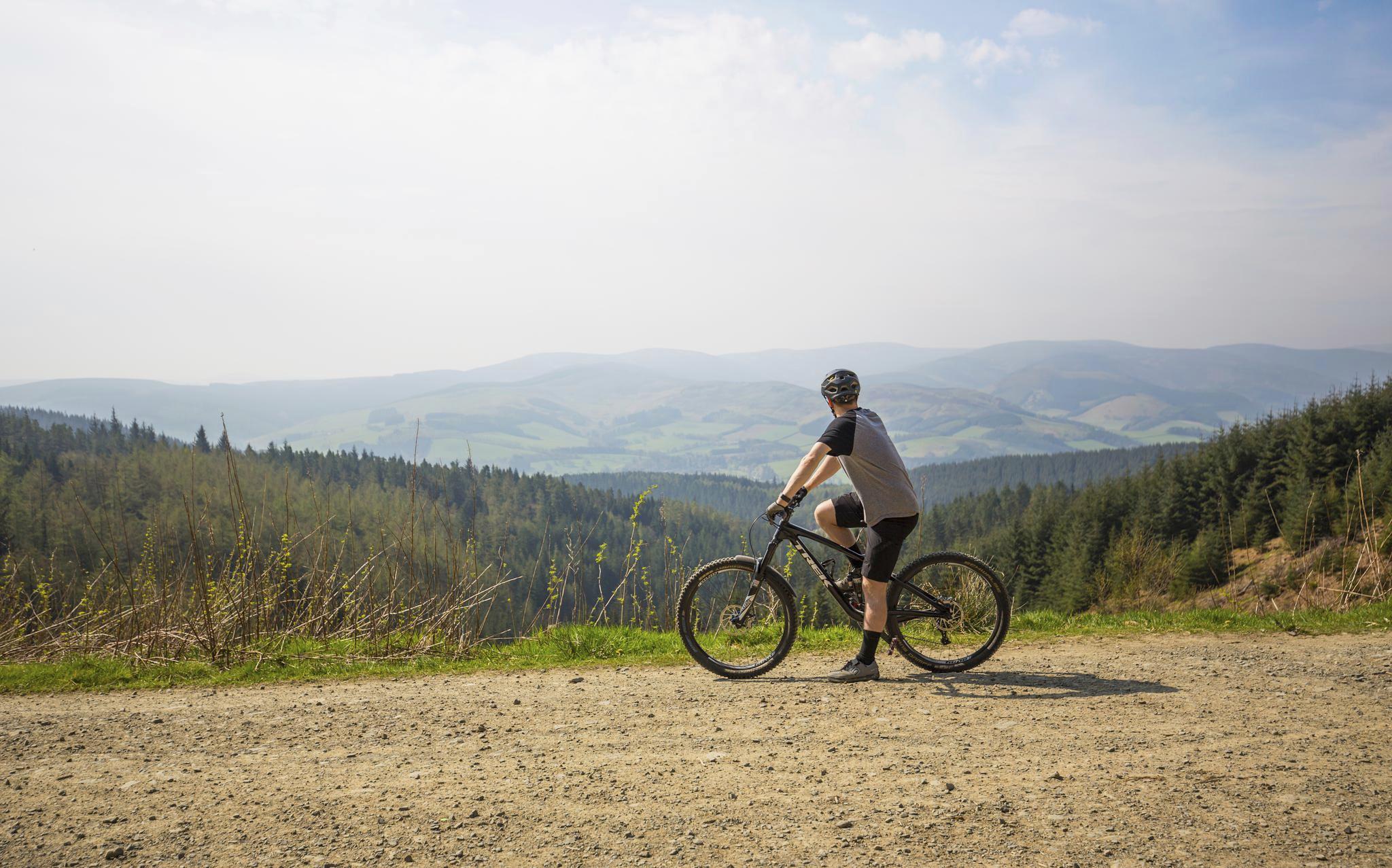 Cyclist stops on path to look over view of the hills beyond.