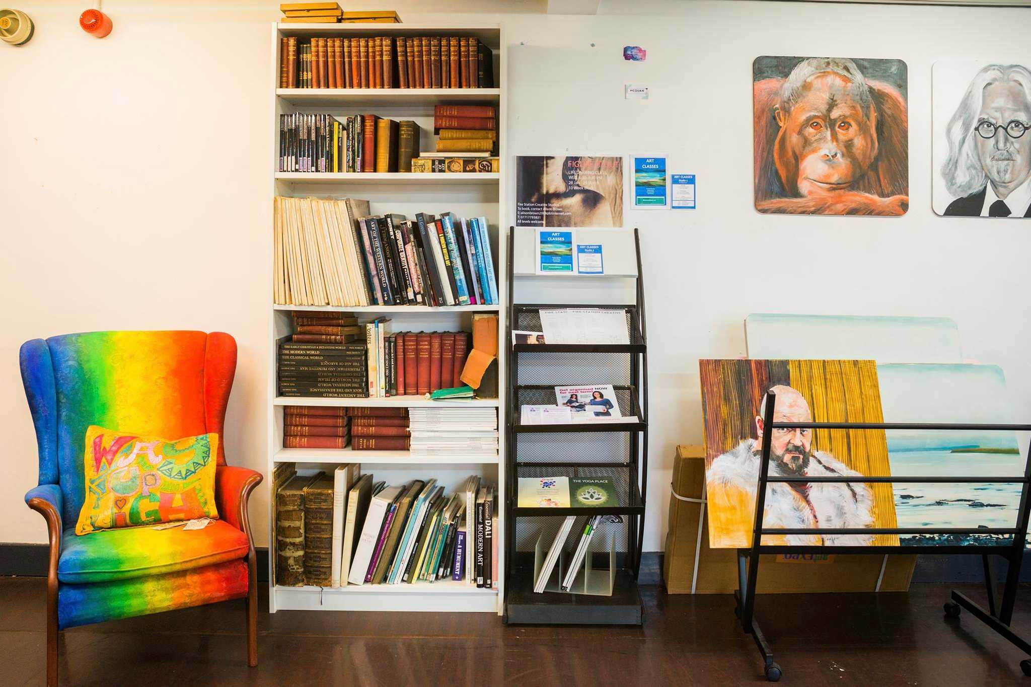 Books and paintings are displayed next to a brightly coloured armchair