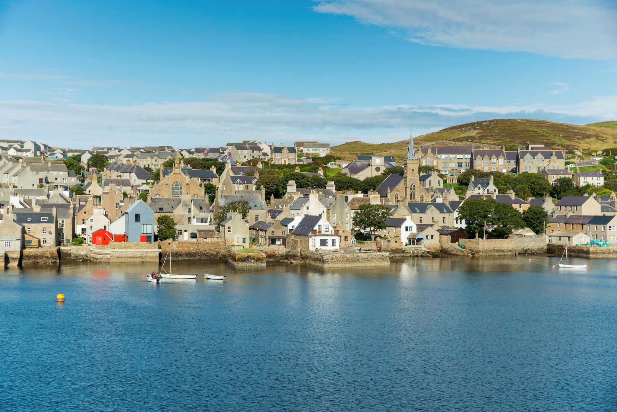 A small town sits by the sea with low hills in the background