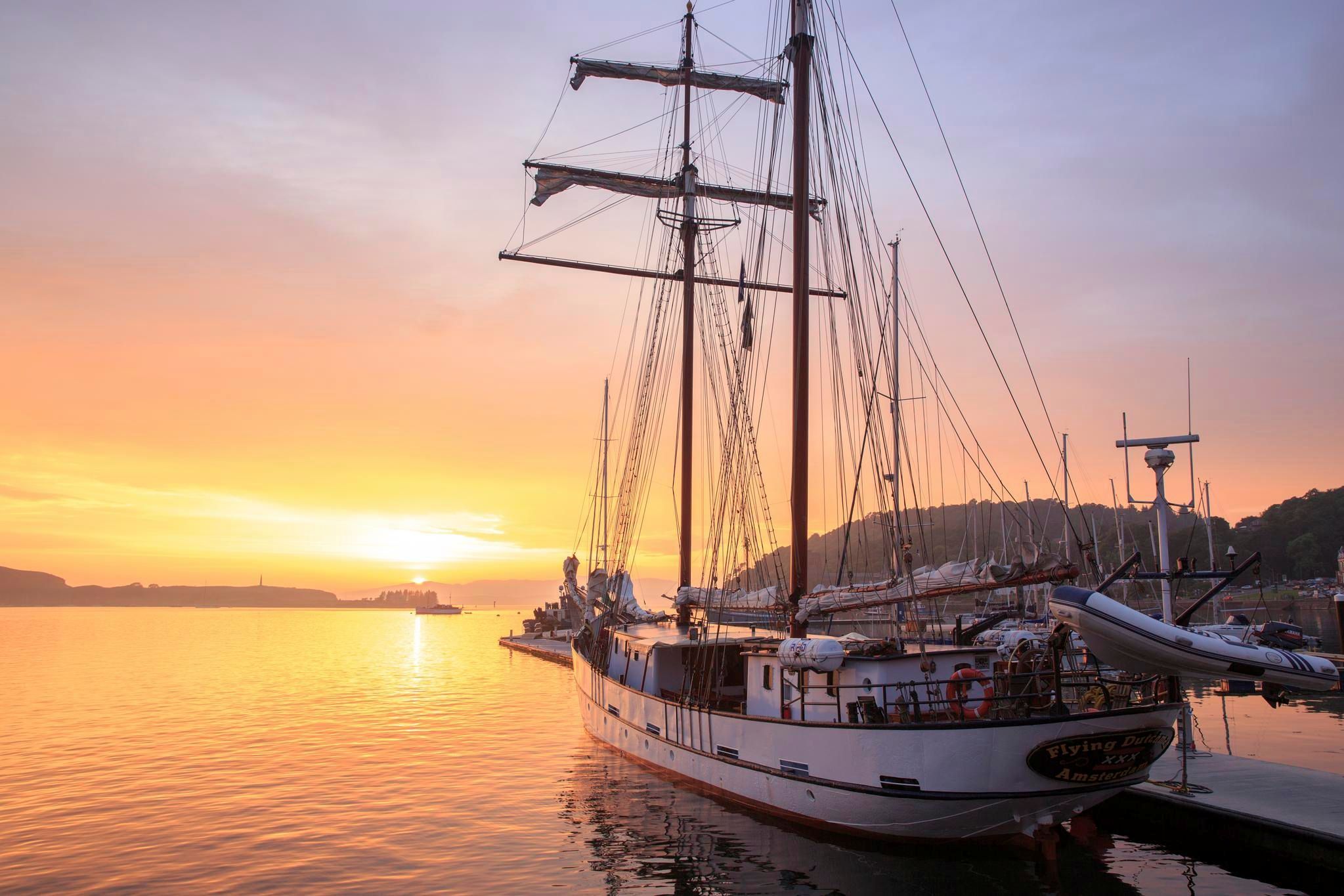 Sun is setting over distant hills casting atmospheric light of boats in the harbour