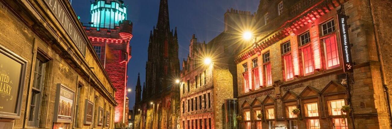 The buildings around the cobbled Royal Mile, lit up in red and blue colours at night