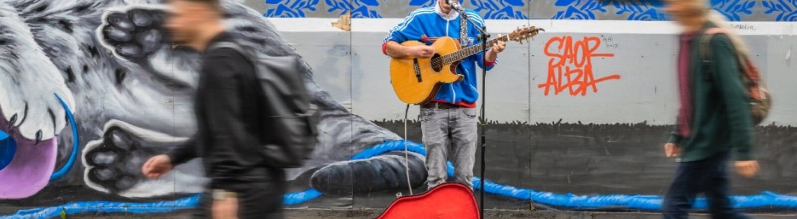 Ein Straßenmusiker mit Gitarre singt, während Menschen vorbeigehen.
