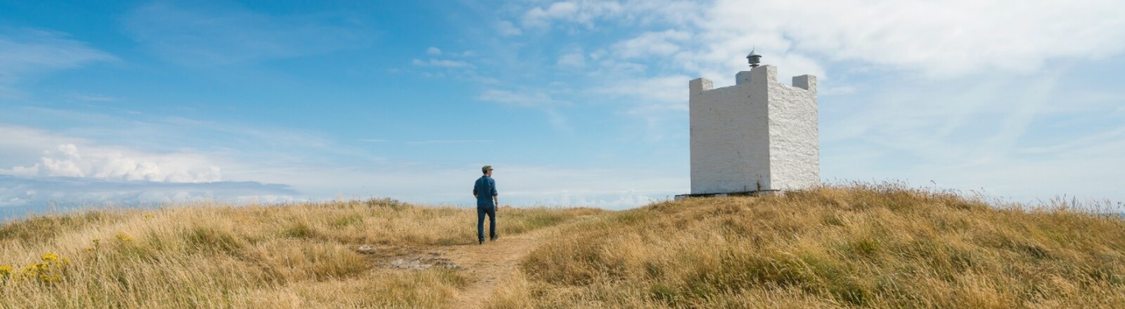 Ein Wanderer steht neben dem Leuchtturm auf der Isle of Whithorn.