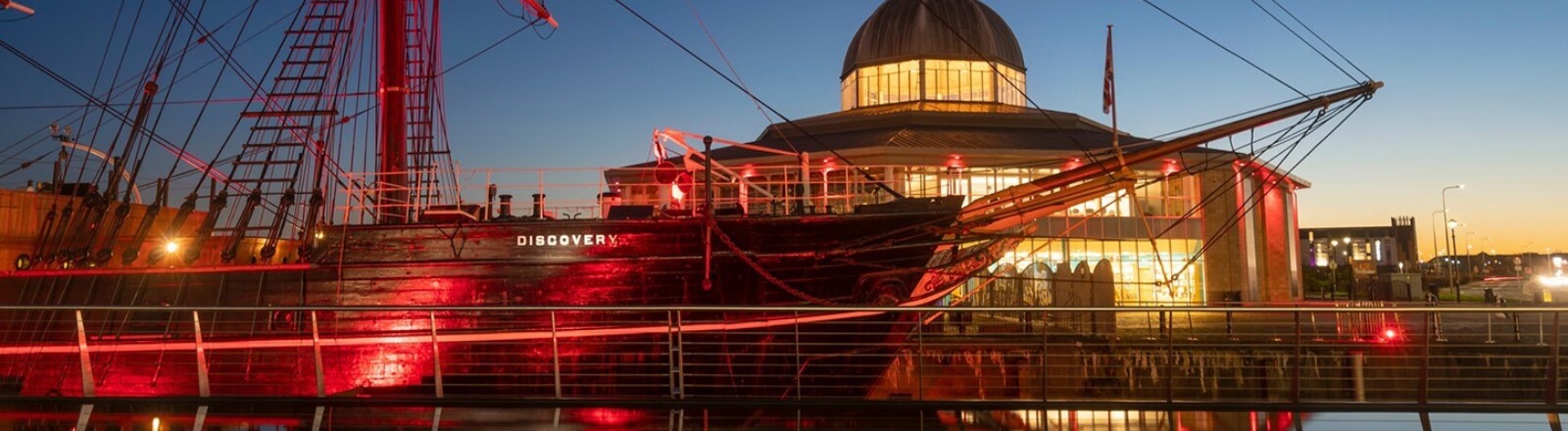 The RRS Discovery sits at Discovery Point, lit up in red as the sun sets