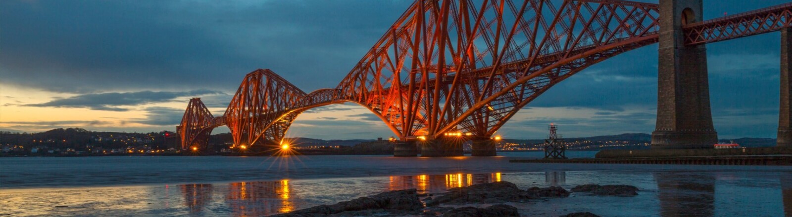 The red Forth Bridge against a night sky, the sun fading behind clouds