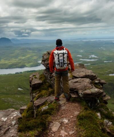 Un uomo si trova in cima a una montagna rocciosa e osserva i fiumi, l'erba e le colline in lontananza