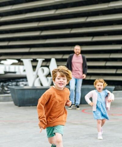 Kids play outside the entrance to the V&A: Dundee as parent looks on