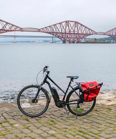 A bike sitting on a pier, the Forth Bridge in the background