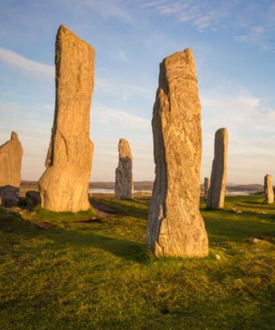 A close up of some of the Calanais Standing Stones on grass against a blue sky