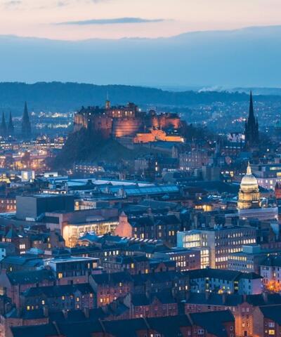 Edinburgh Castle sits in the middle surrounded by buildings lit up as night falls