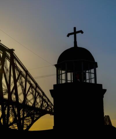 The world's smallest working light tower in North Queensferry in silhouette against the Forth Bridge