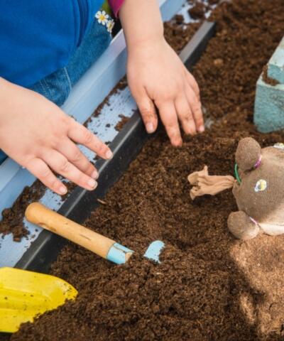 A close up of someone's hands working in some earth with some gardening tools