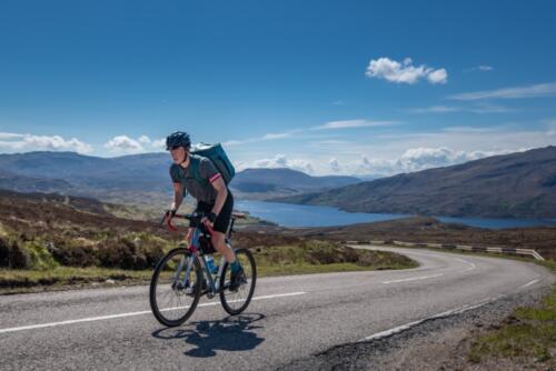 A cyclist travelling along a road next to Loch Assynt on a beautiful sunny day