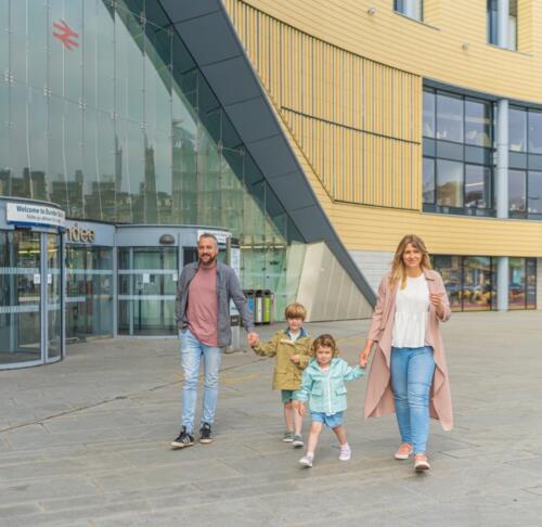 Una famiglia con due bambini cammina sul marciapiede davanti alla stazione ferroviaria di Dundee
