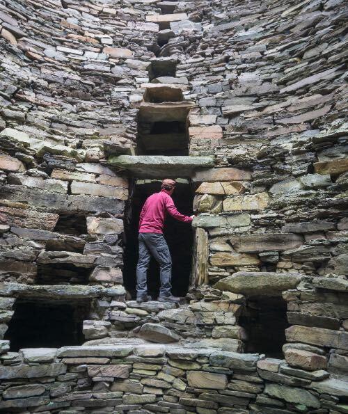 Un uomo esplora l'interno della casa di pietra di Mousa Broch