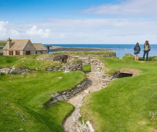 Due spettatori ammirano Skara Brae, parte del sito del patrimonio mondiale Heart of Neolithic Orkney presso la baia di Skaill, nelle Orcadi