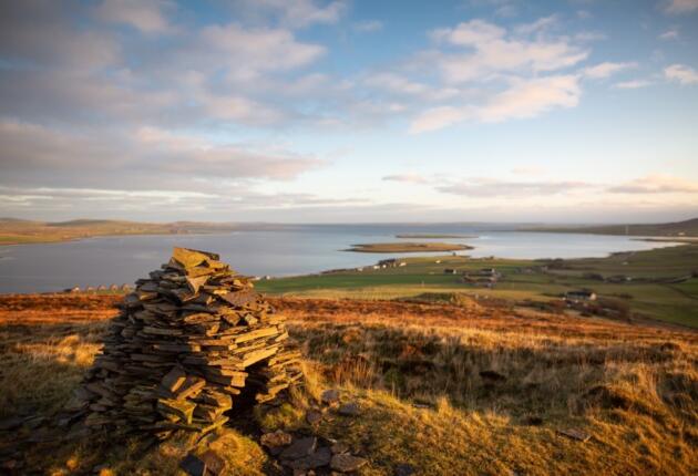 Cuween Chambered Cairn made of stones, sits on the top of Cuween Hill as the light fades against the water