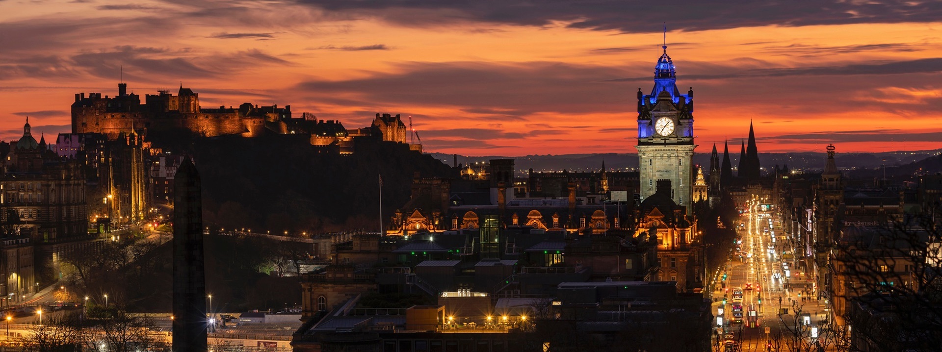 Panorama von Edinburgh bei Nacht mit der Princes Street, dem Balmoral Hotel, Edinburgh Castle und weiteren Gebäuden.
