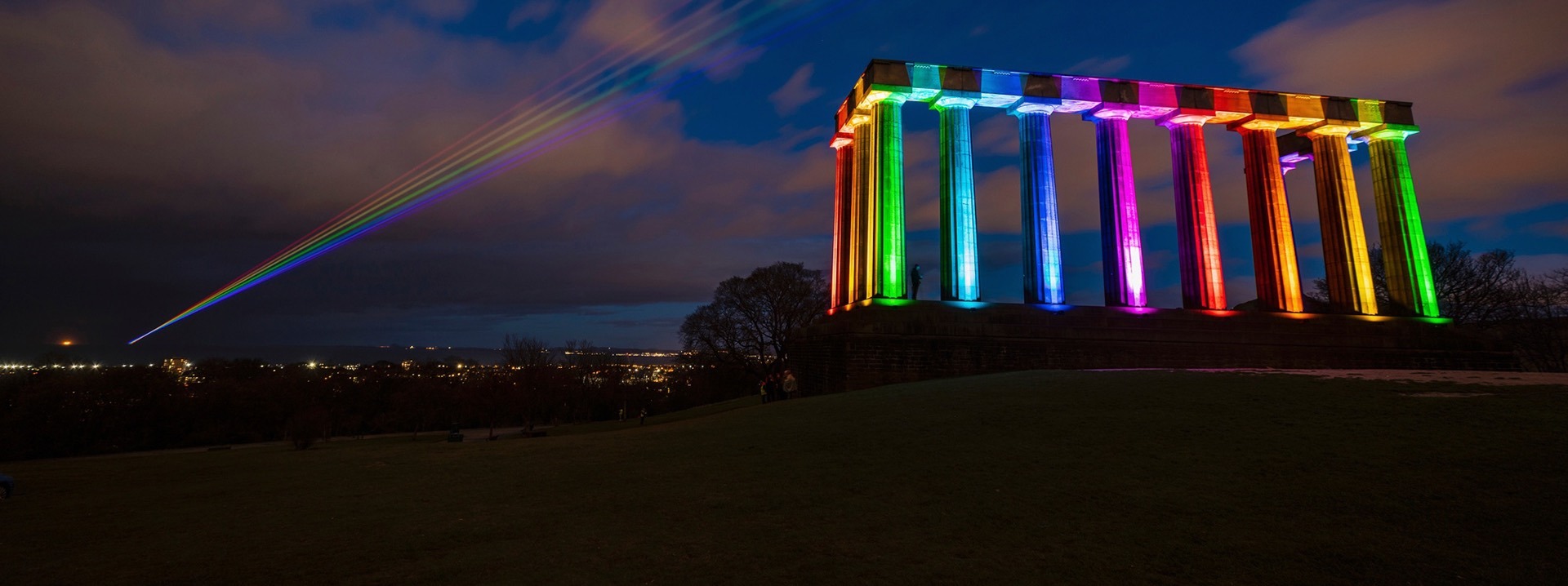 Das National Monument of Scotland wird bei Nacht in Regenbogenfarben angestrahlt.