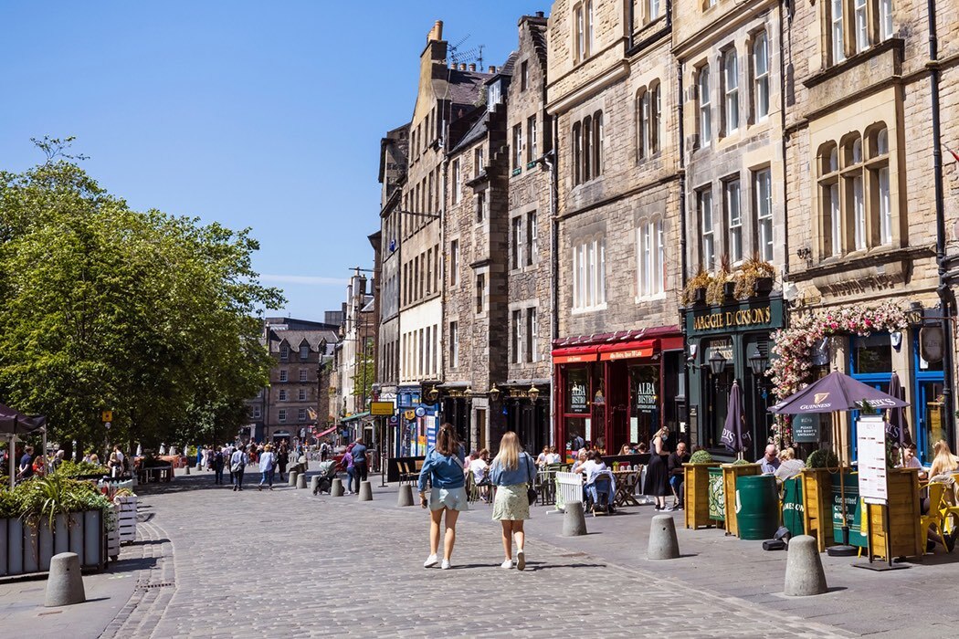 The two women walk down the  Grassmarket in summer. The Grassmarket is located directly below Edinburgh Castle and forms part of one of the main east-west vehicle arteries through the city centre.