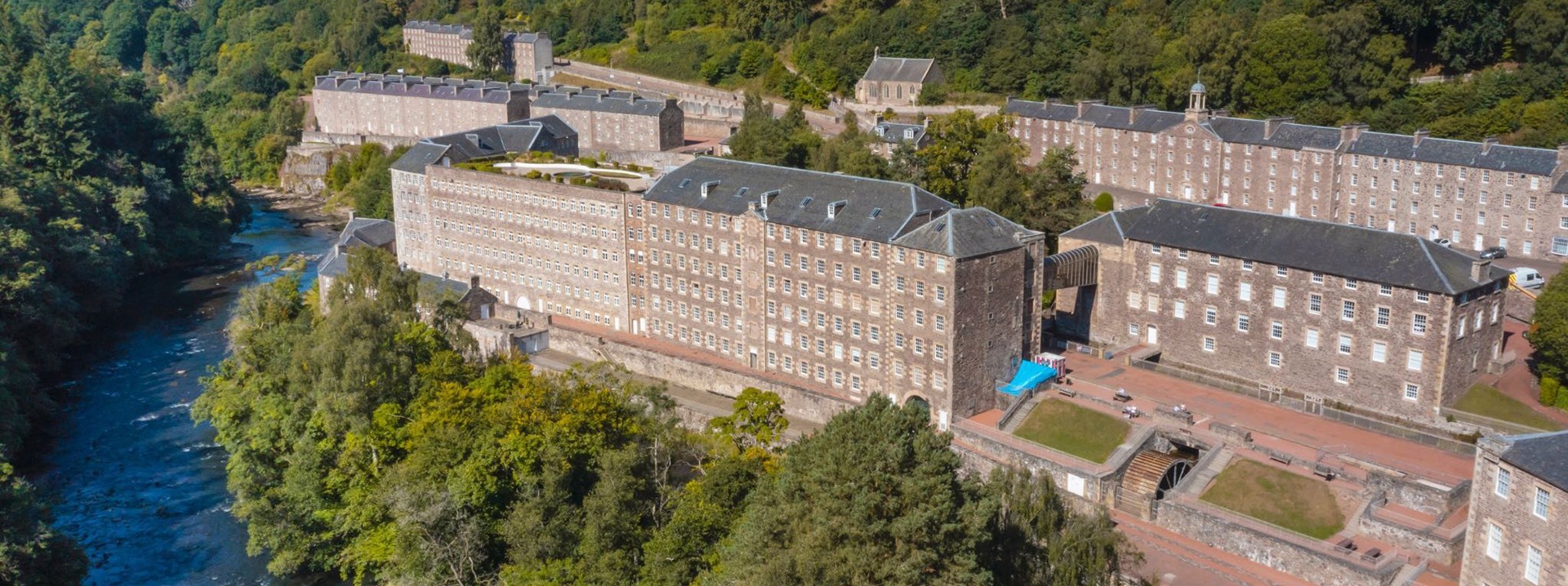 An aerial shot of the buildings of New Lanark, surrounded by trees and the river