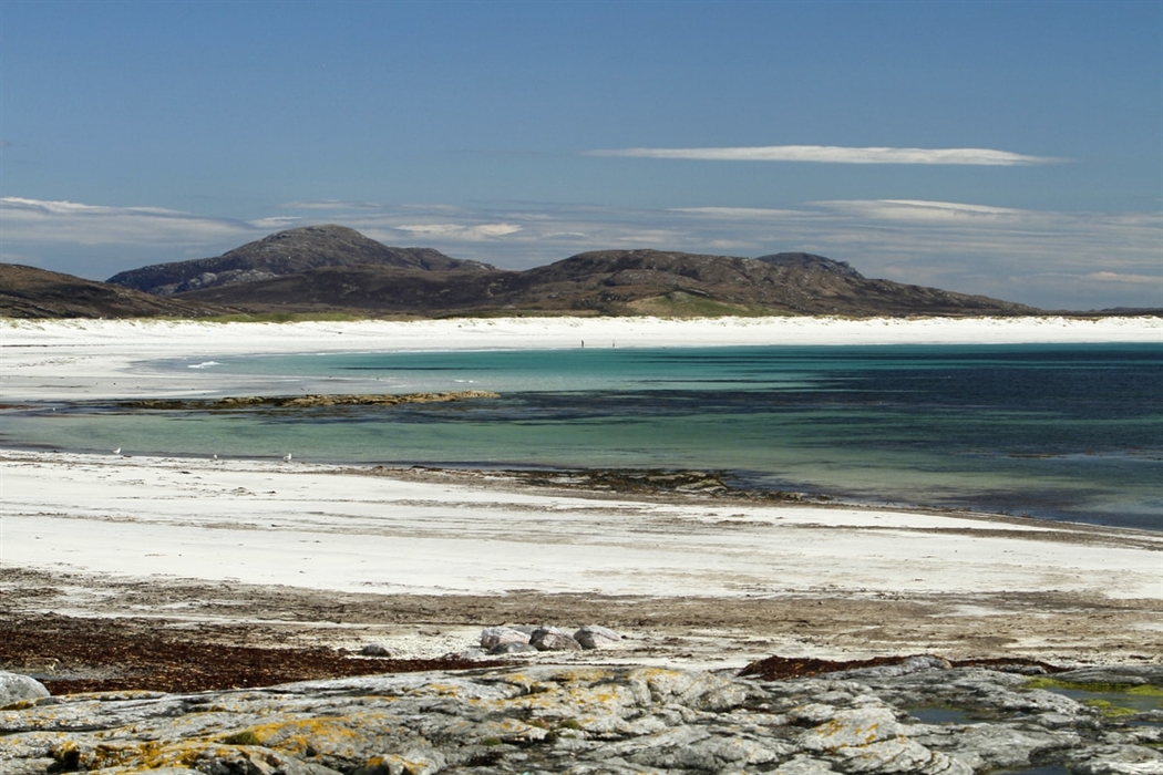 The beach near Bornish on the west coast of South Uist. Pure white sand in a wide sweeping bay and deep turquoise waters, with mountains beyond.
